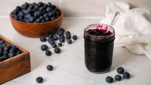 A jar of blueberry jam on a counter with blueberries.