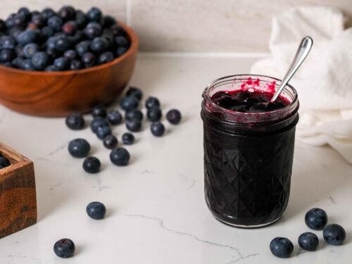 A jar of blueberry jam on a counter with blueberries.
