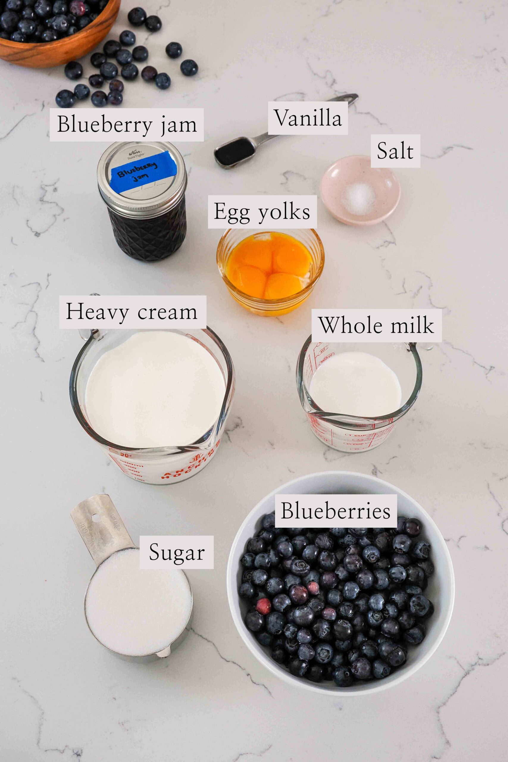 Ingredients needed to make blueberry ice cream on a quartz counter.