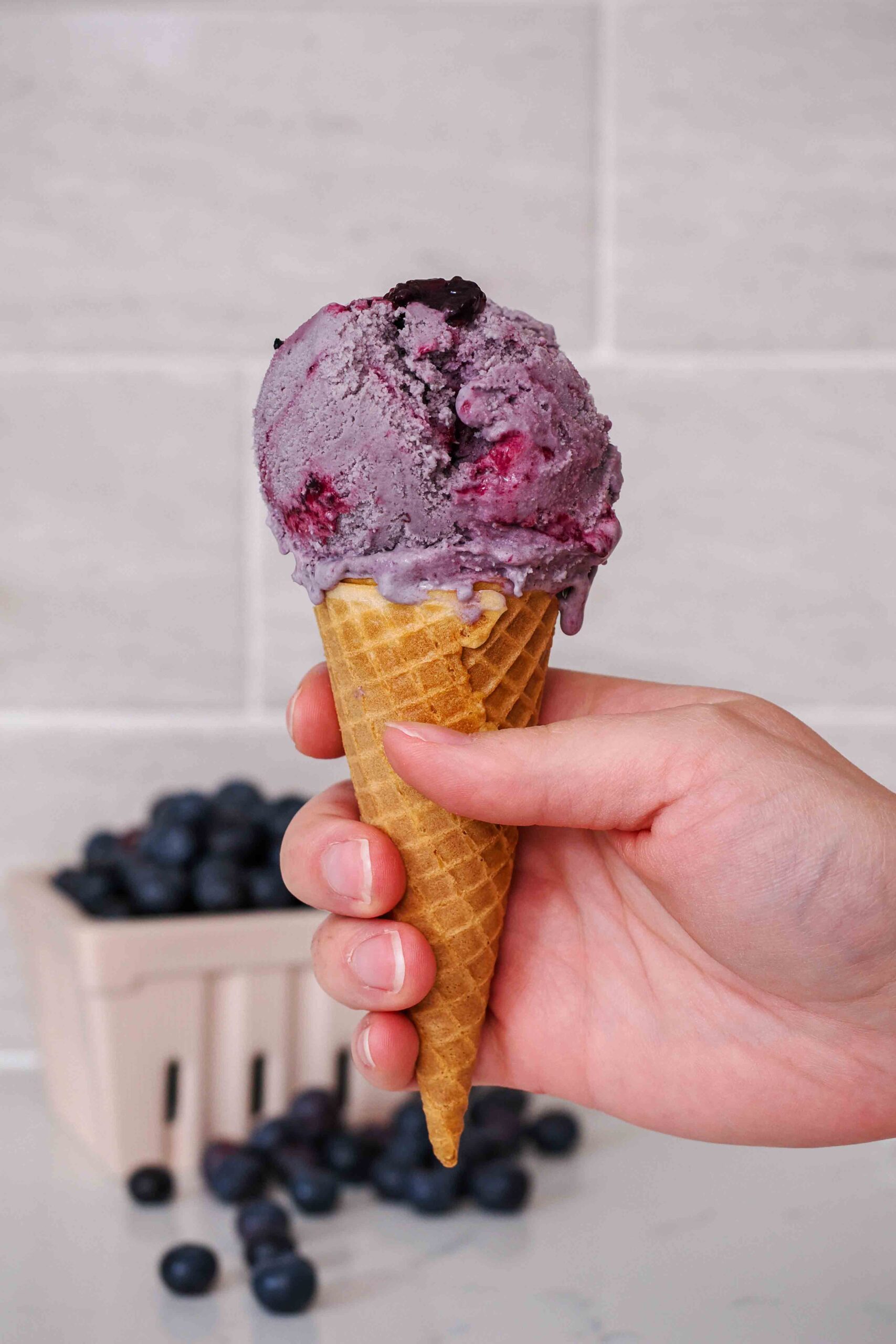 A hand holds up an ice cream cone with blueberry ice cream.