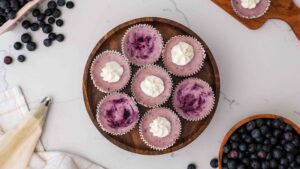 An overhead view of mini blueberry cheesecakes on a wooden cake stand.