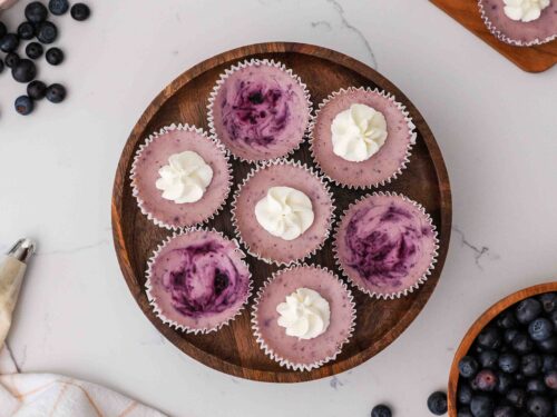 An overhead view of mini blueberry cheesecakes on a wooden cake stand.