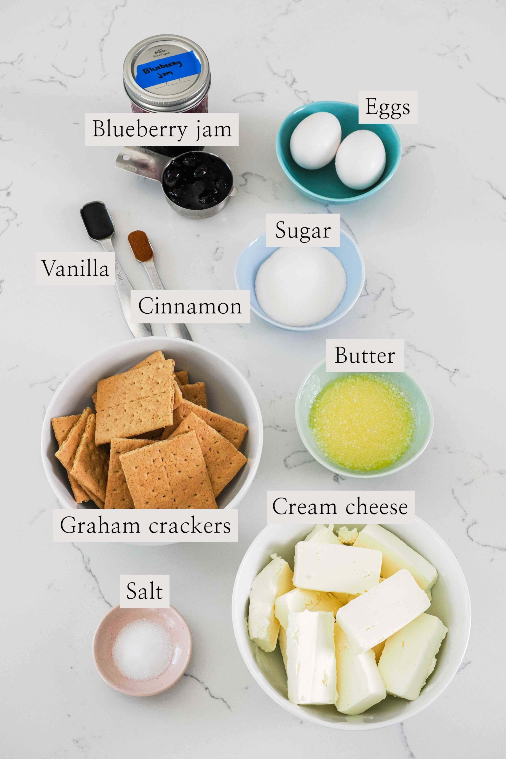 Ingredients needed to make mini blueberry cheesecakes on a quartz counter.